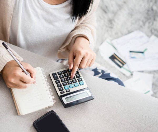 woman writing a list of debt on notebook calculating her expenses with calculator with many invoices , female hand doing accounting
